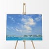 Fresh Air Skies Oil Painting Sky Landscape by Andrew Gaia on easel. Fluffy clouds cascade over a blue green bay as the ship prepare for the beautiful day.
